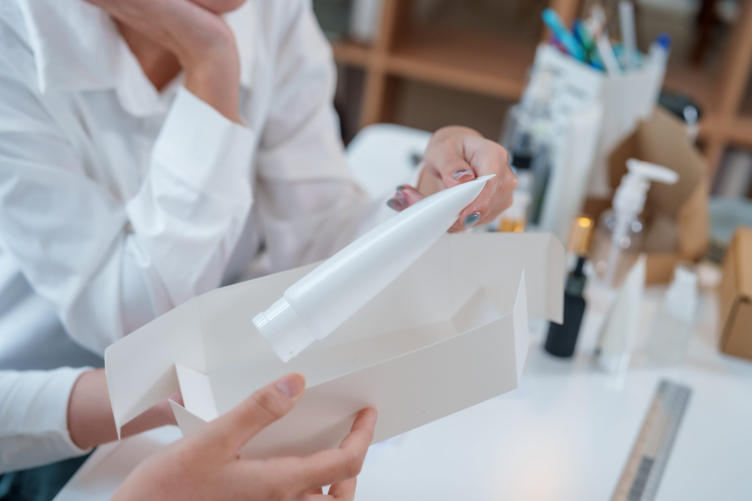 Person examines cosmetic product inside its packaging, showcasing design and development process. This moment highlights importance of market research in creating appealing products