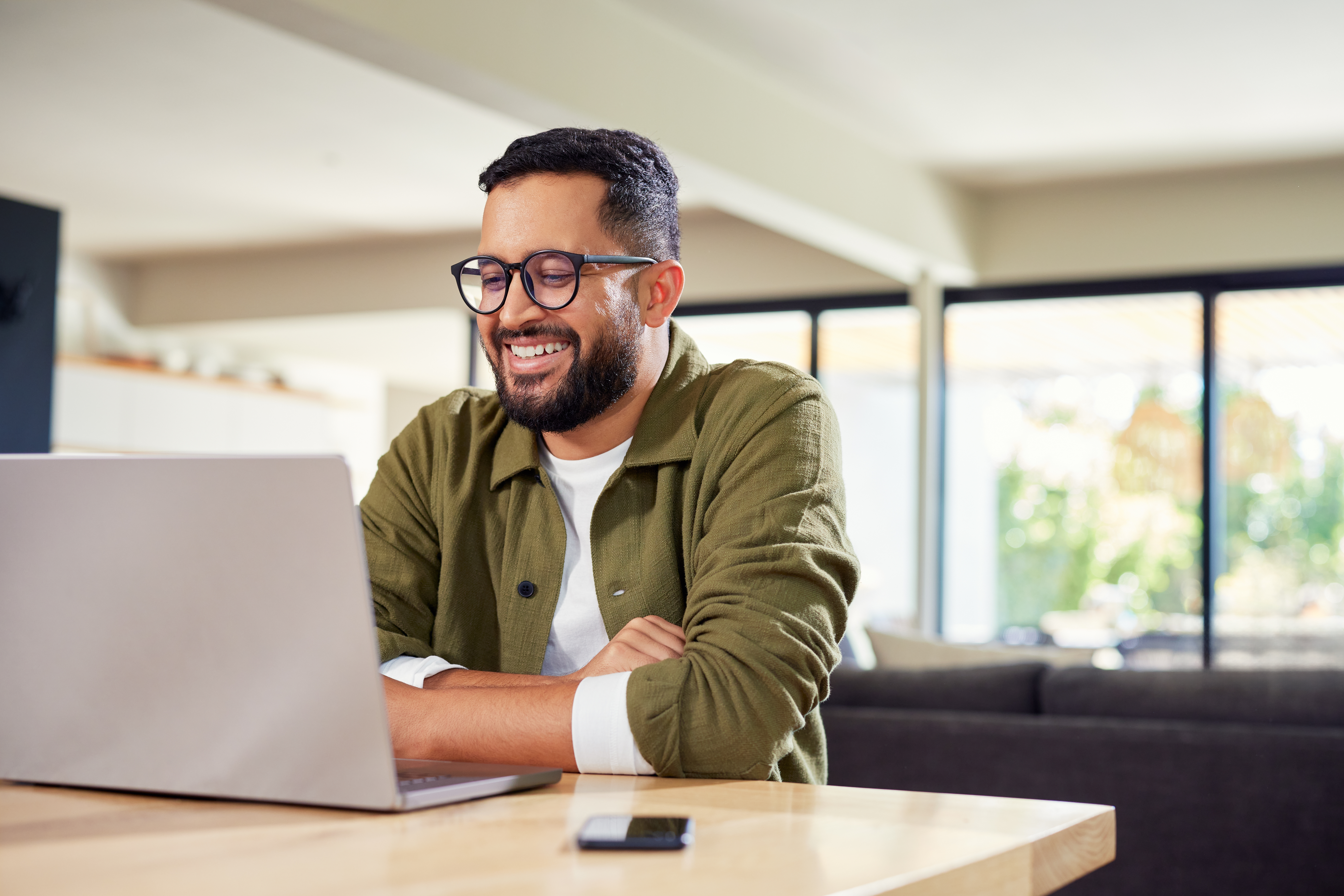 Smiling young man sitting at home while using laptop. meeting online at home while using laptop. Happy man wearing eyeglasses while using laptop during work from home with copy space.
